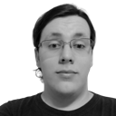 Monochromatic photo of a caucasian male in his early twenties, slightly overweight, shoulder-length hair tied at the back, wearing slightly crooked square-framed glasses and a black T-shirt upon an empty background.